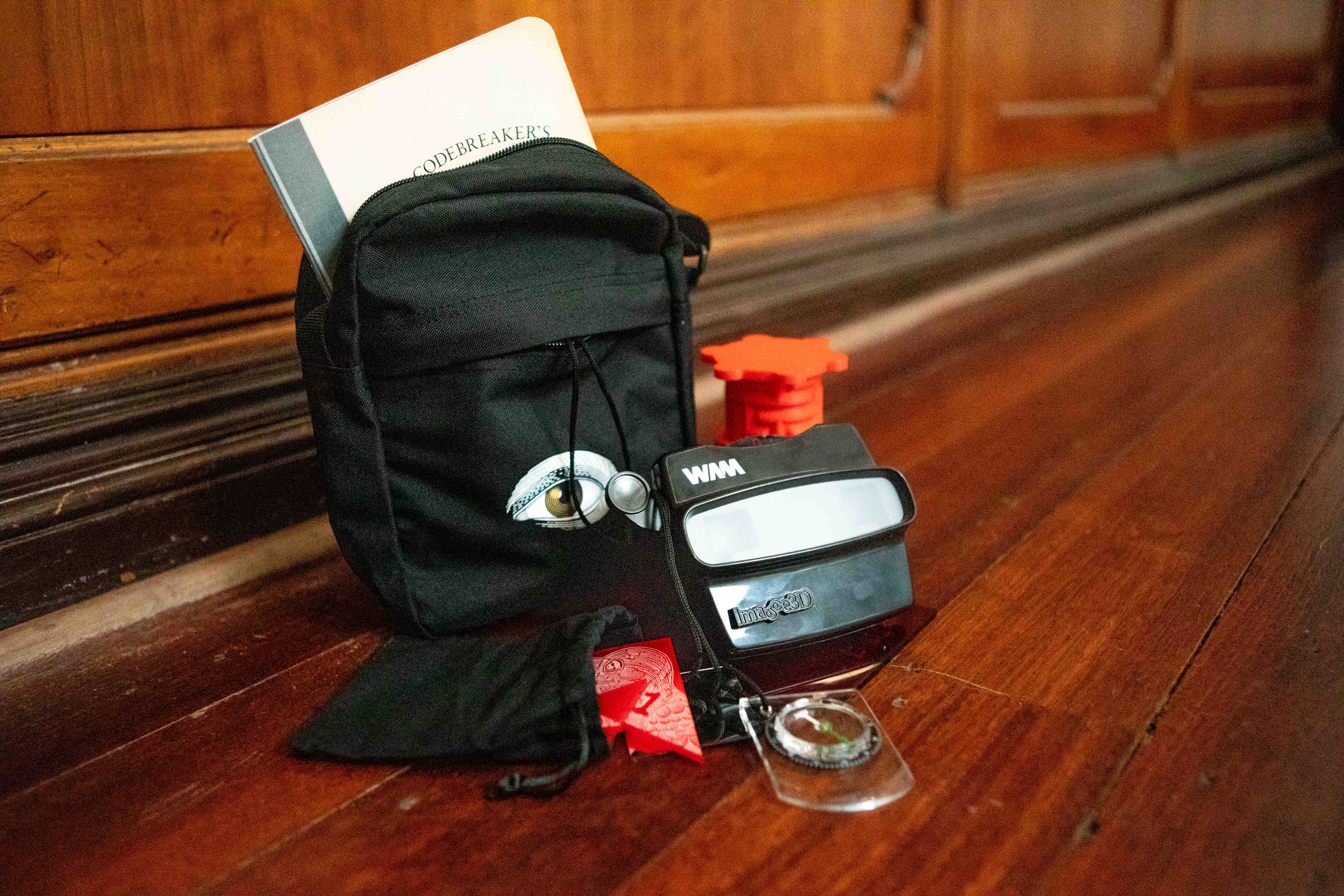 The Codebreakers kit, featuring a little black bag, jigsaw pieces and glasses, lies on a wooden floor.