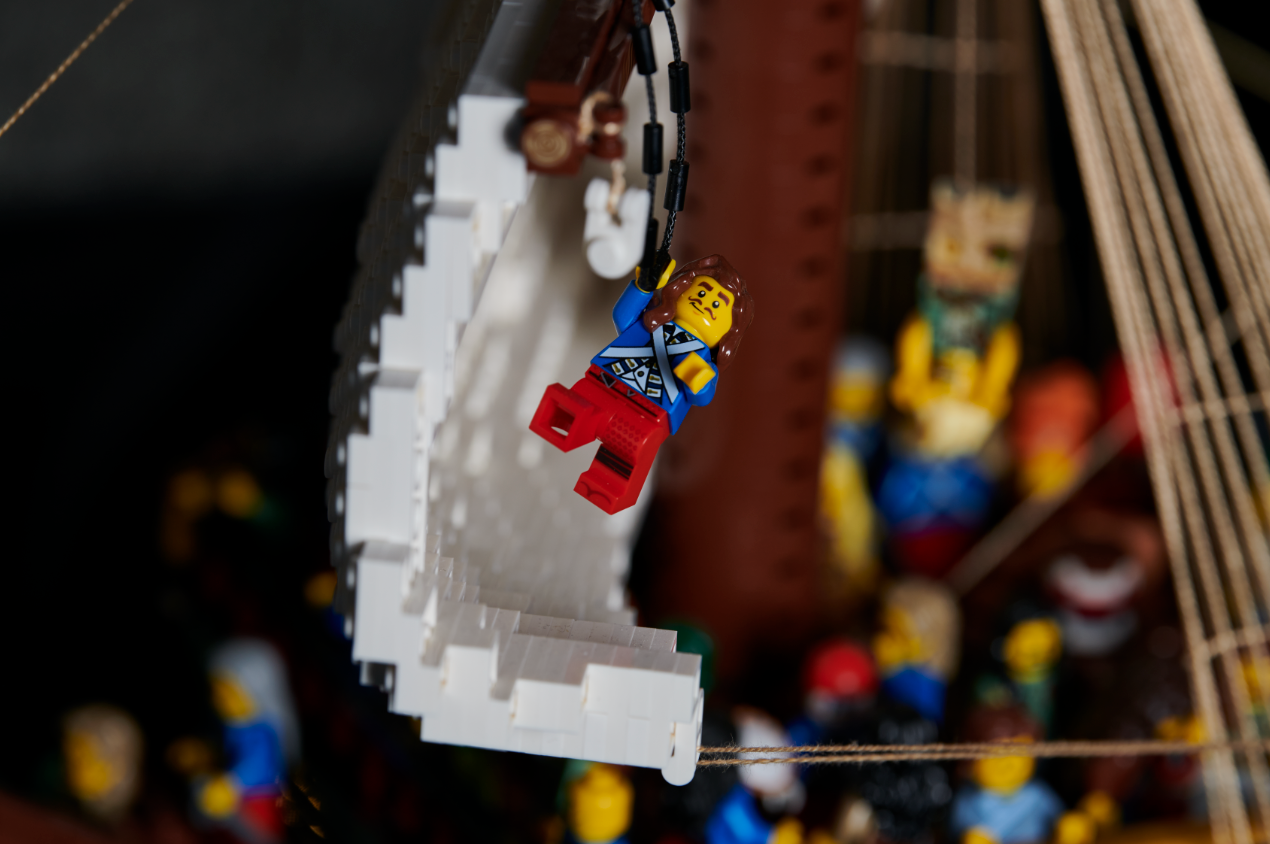 a LEGO MAN WITH A BEARD HOLDS ONTO A STRING, SWINGING FROMA LEGO BOAT