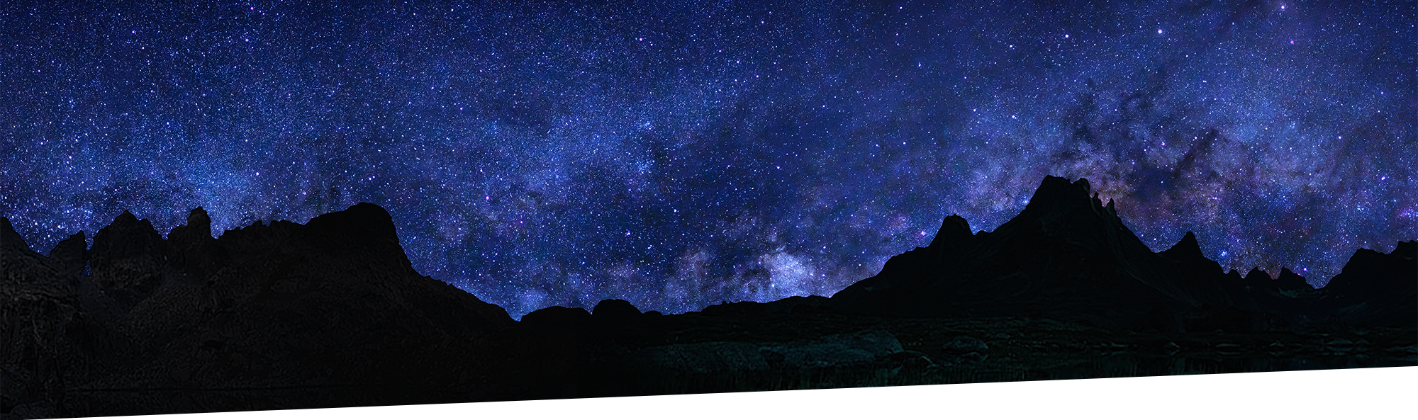 Mountains are silhouetted against a starry night sky
