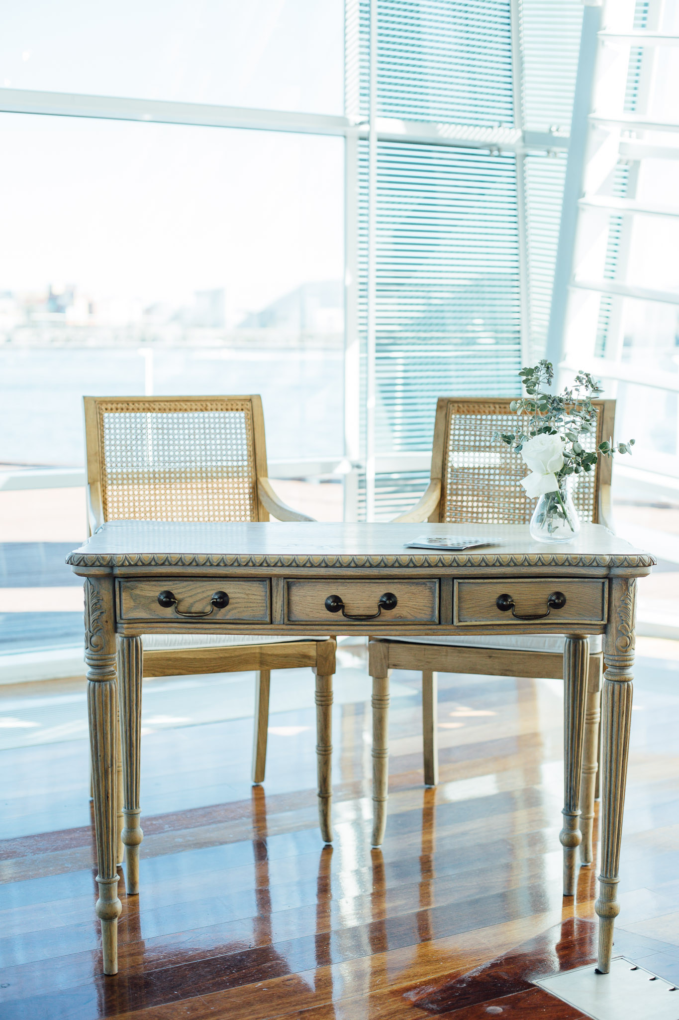 Two wicker chairs in front of a vintage-style table with a large, well-lit window in the background