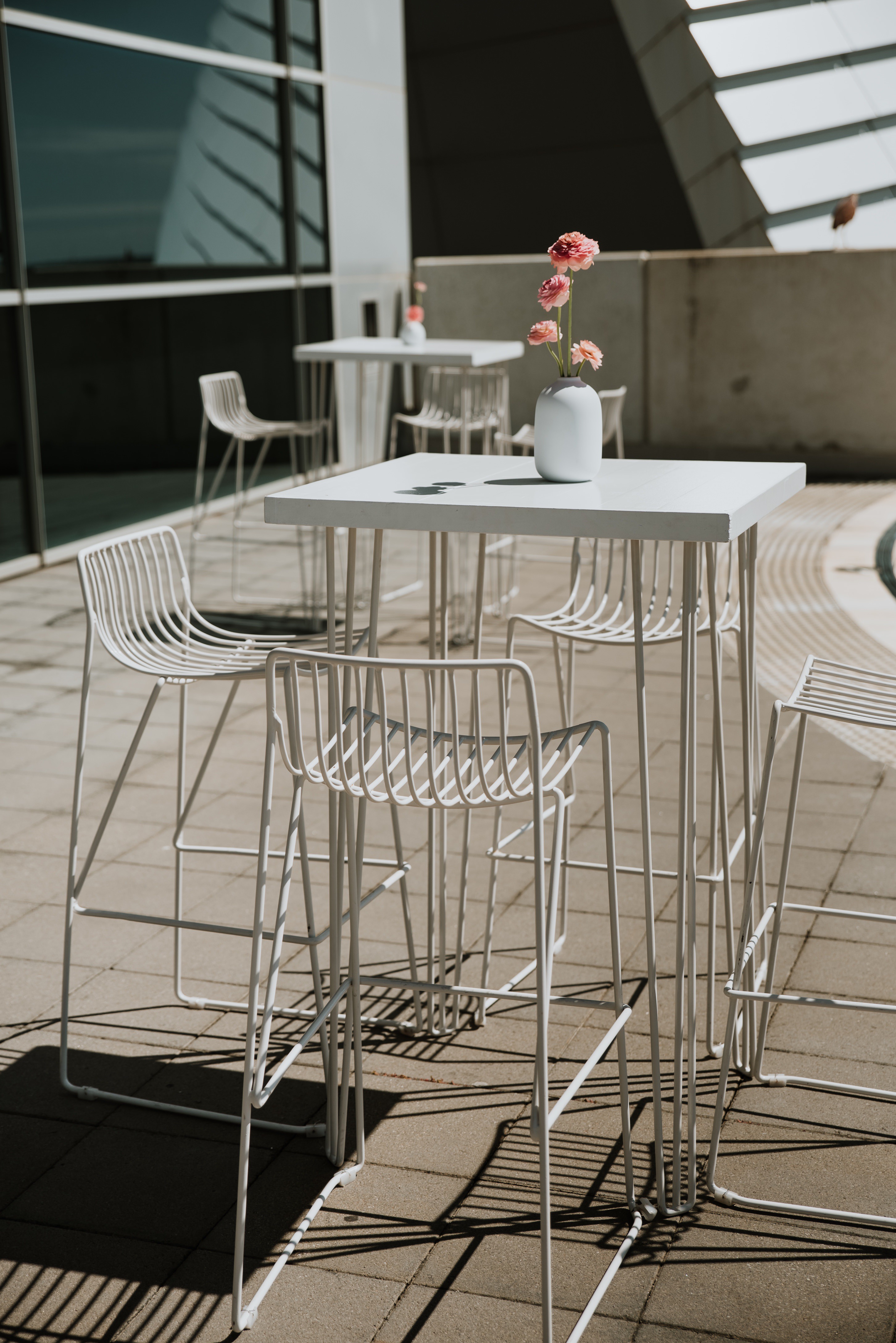 Thin-wired, high-legged chairs beside a table with pink flowers in a white vase, on the balcony of the Maritime Museum