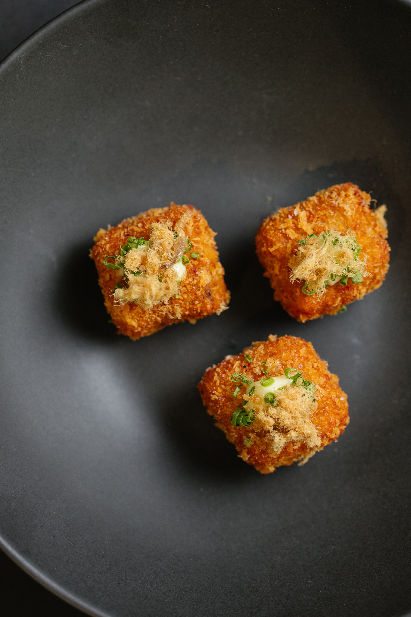 Three small golden brown croquettes on a black plate with a green garnish
