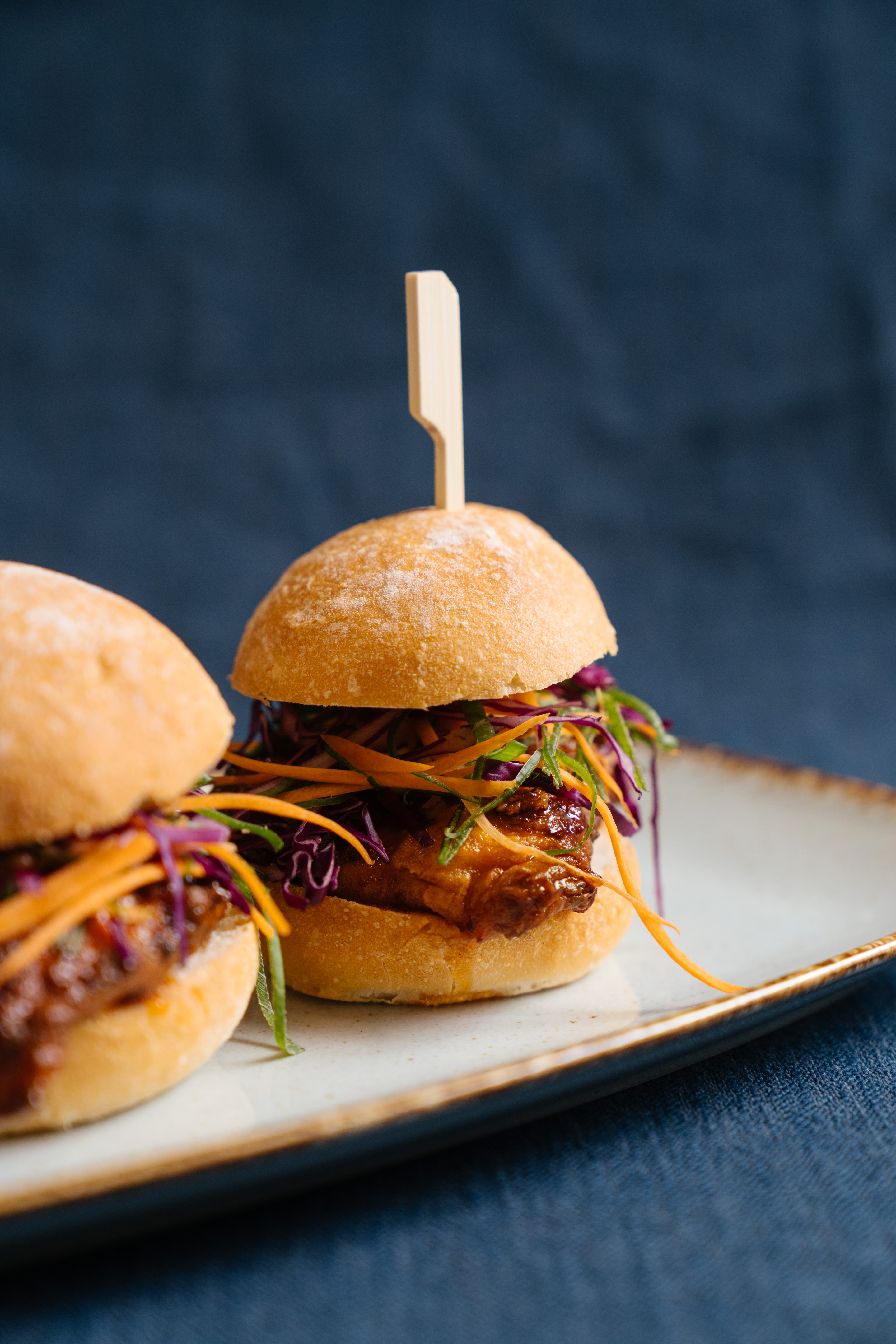 Two small sliders with a wooden skewer with shredded carrot and cabbage and a piece of golden chicken breast