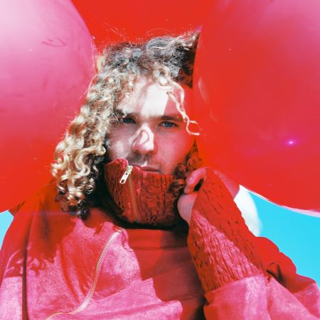 Image of singer songwriter Noah Dillon wearing read surrounded by red balloons.