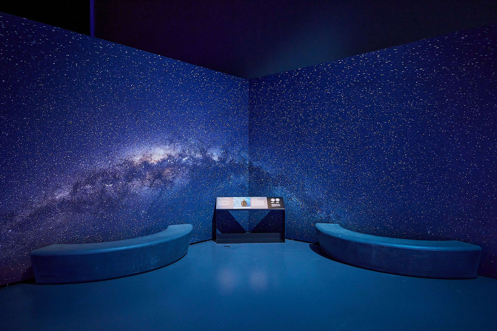 Tranquil space inside the exhibition with a wall and bench with a blue galaxy decal behind it, positions near the large moon installation.