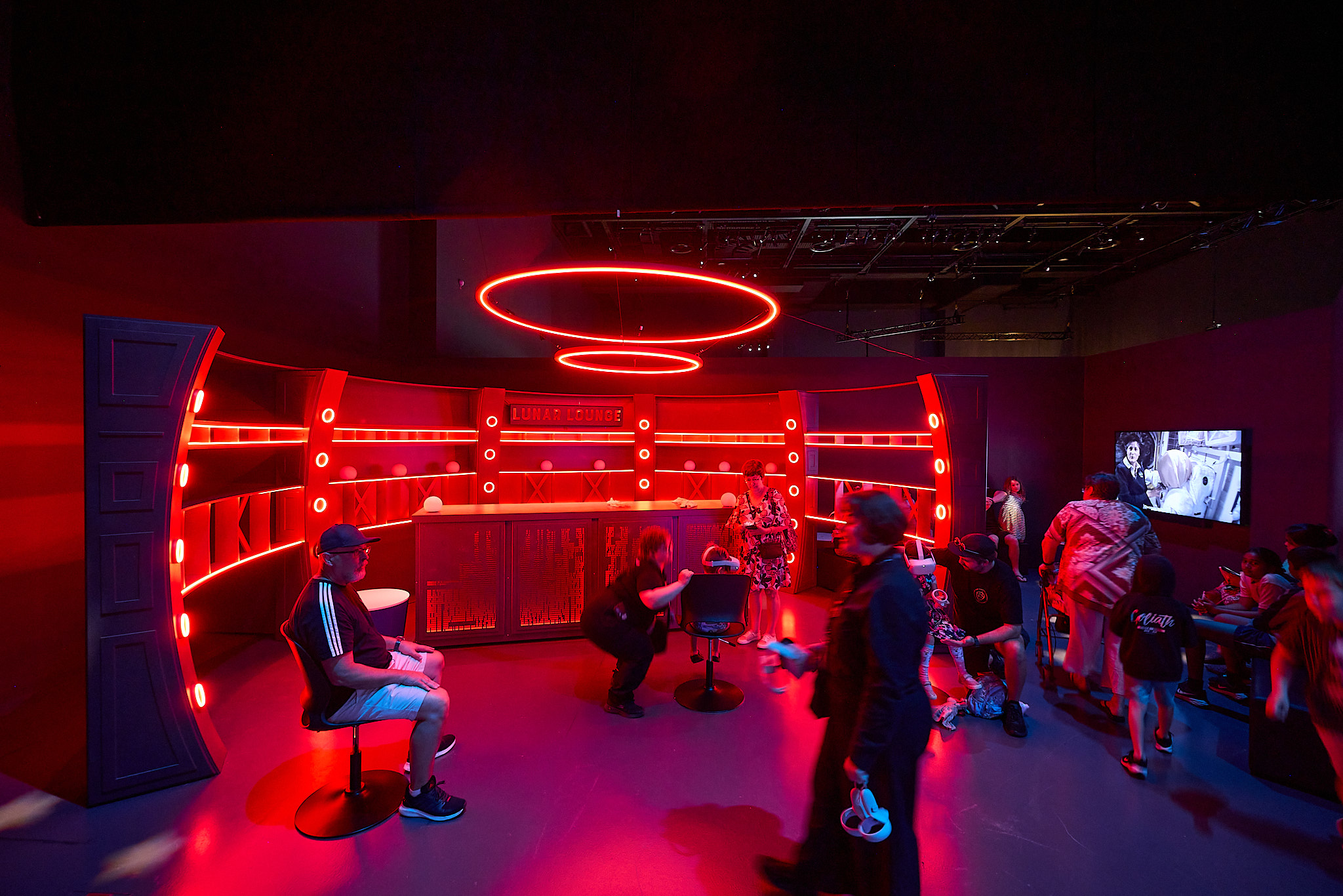 A young child experiencing virtual reality through a headset, holding controllers in a red lit room. 