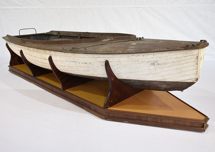 The open built Endeavour is a snub-nosed, carvel planked 14-foot wooden dinghy. It can be rigged as a sloop or a gaff, and has a centreboard, foredeck, and side decks. The hull to the waterline is painted white, while the deck, side benches and underside of the hull are painted brown. The original sail insignia shows the letter “E” inside a red and white diamond.