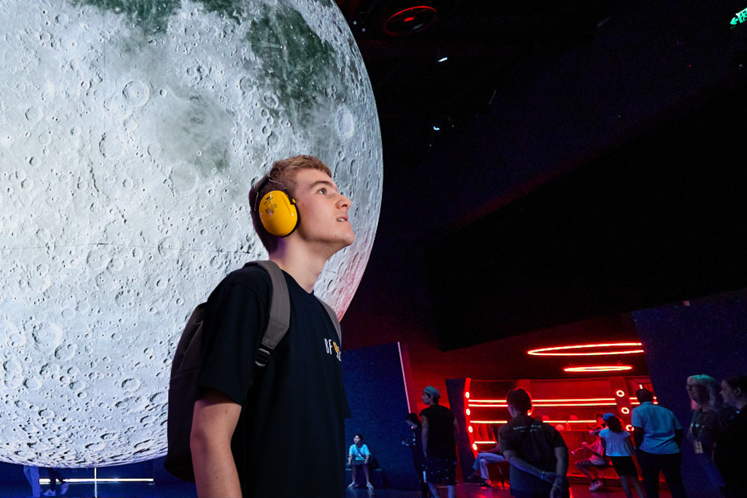 A person with short blonde hair wearing headphones gazes at the moon in the exhibition space. 