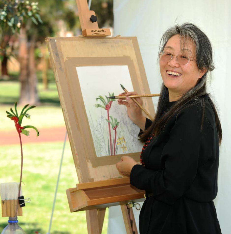 Portrait photograph of artist Jane Li painting a kangaroo paw