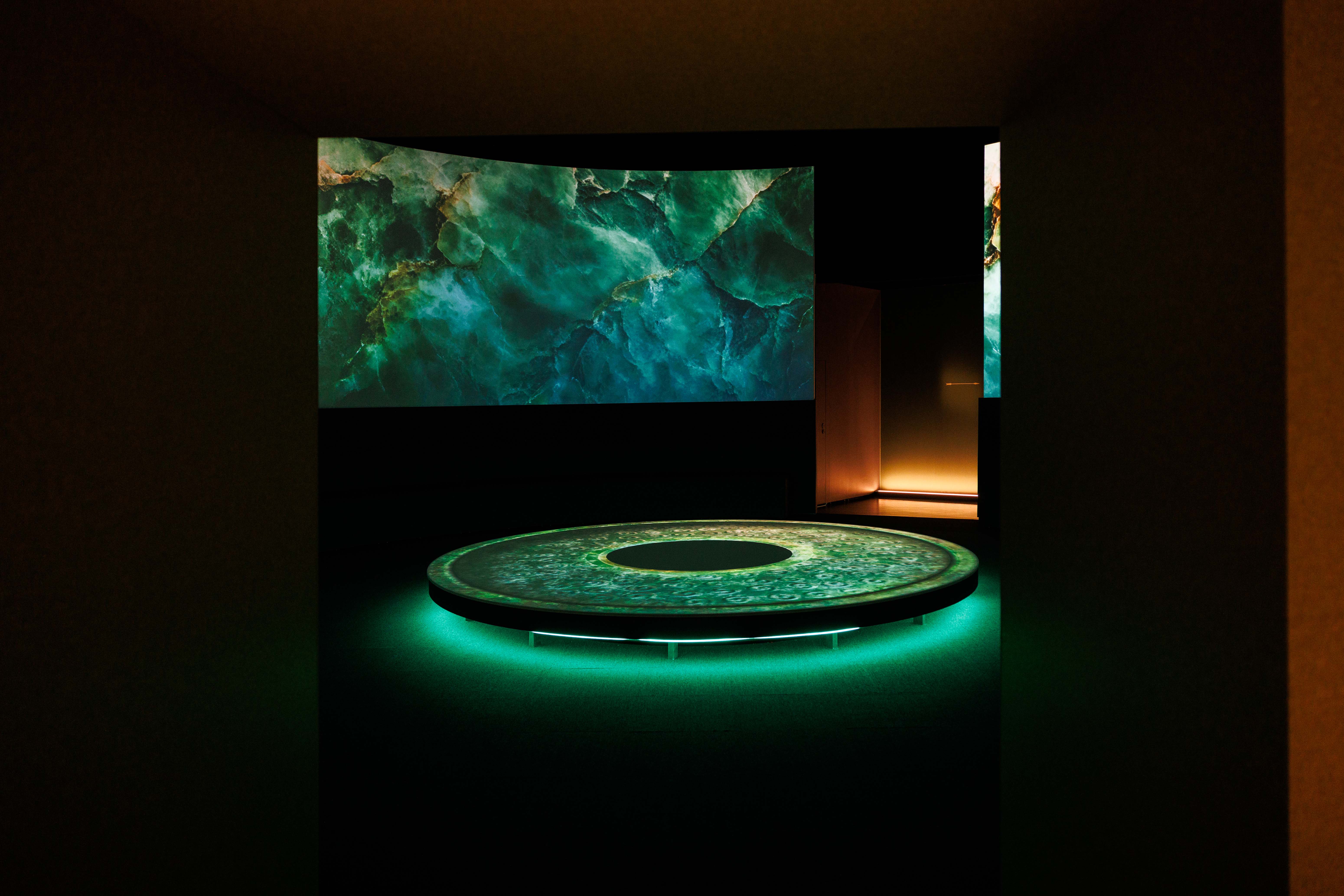 A dark room with a glowing green circular platform and abstract marbled projections on the walls.