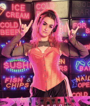 DJ Projext Bexx infront of DJ decs and neon signs