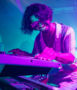 Parvan Kumar (male) playing keyboard in a club environment with blue and pink lights
