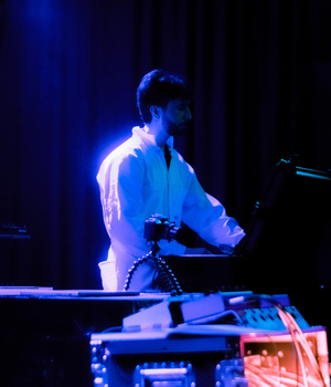 Man in white suit in front of musical decks with blue light on him.