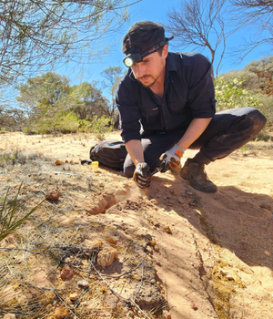 Man kneeling on ground with head-torch and gloves on.
