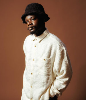 Man in white shirt with bucket hat infront of brown screen