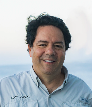 Man with brown hair smiling, wearing a shirt that says OceanX
