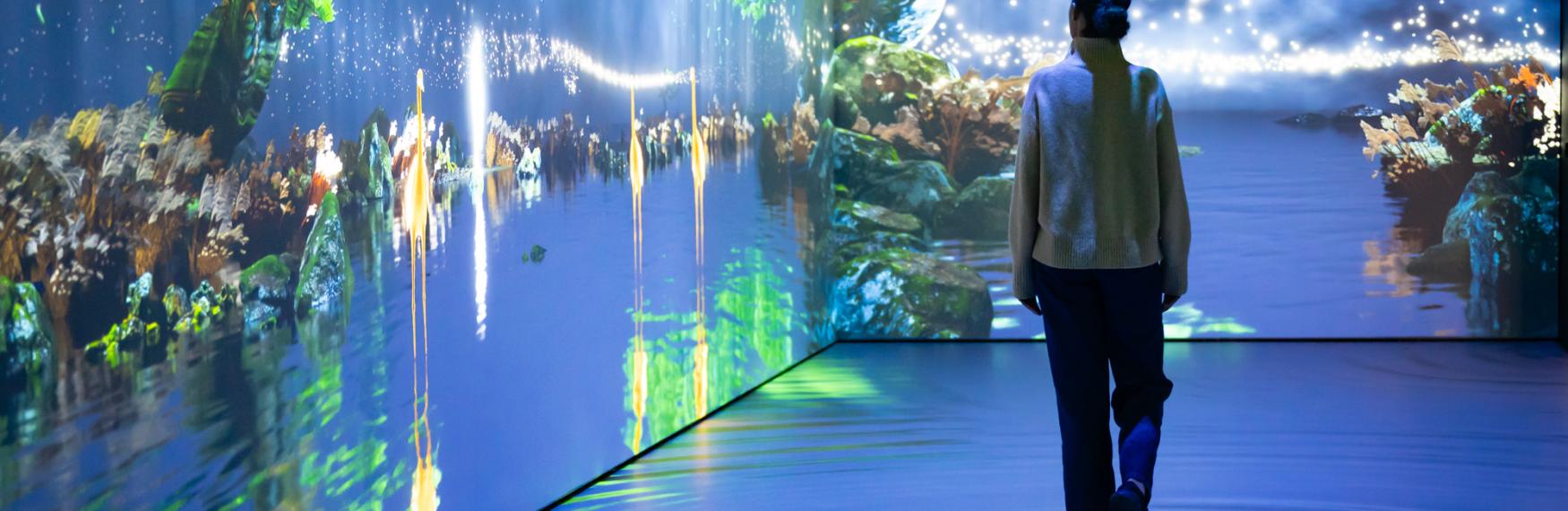 Person in immersive digital projection of trees and water.