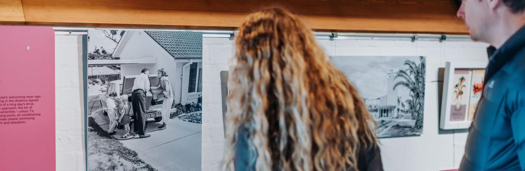 A man and a woman look at a black and white vintage photograph on a Museum wall.
