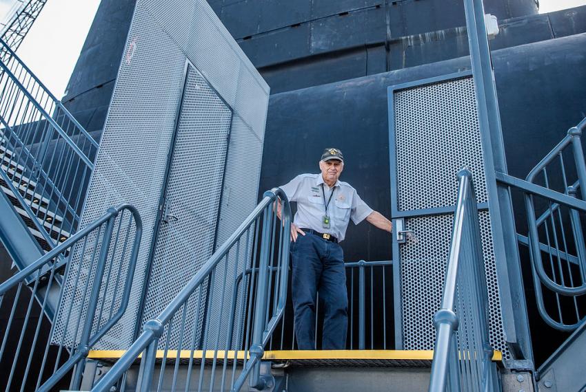 A tour guide stands at the top of a staircase, ready to bring visitors inside the HMAS Ovens