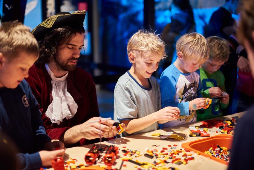 A group of children build LEGO models with a facilitator in pirate costume