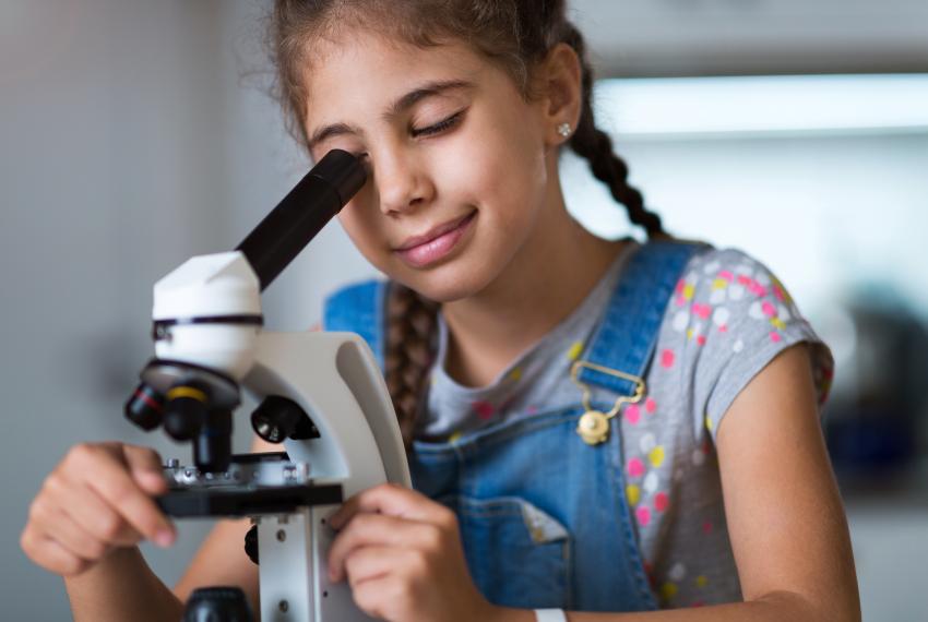 A young girl looks intently down the lens of a microscope