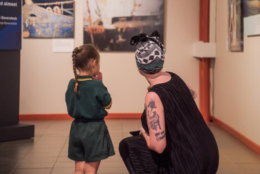 An adult kneels down to talk to a child in a museum gallery