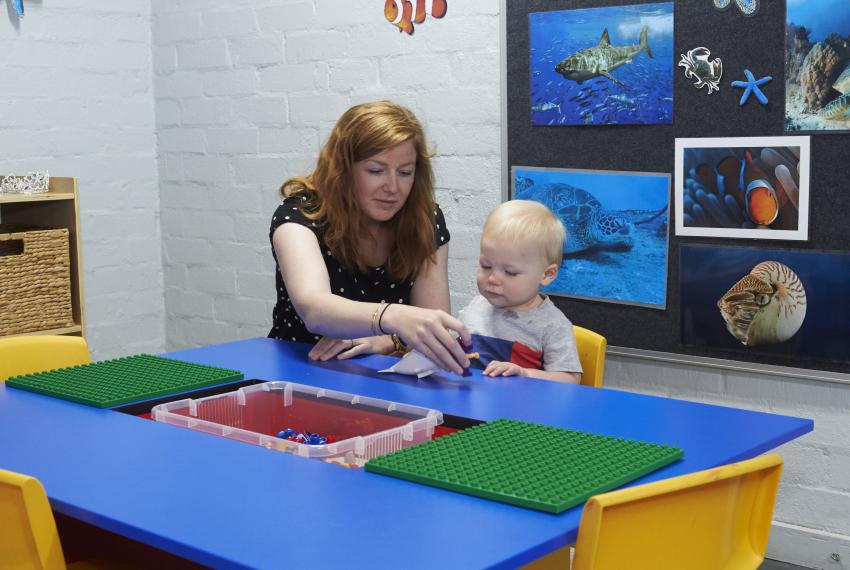 An adult and a child play with toys at a brightly coloured classroom table