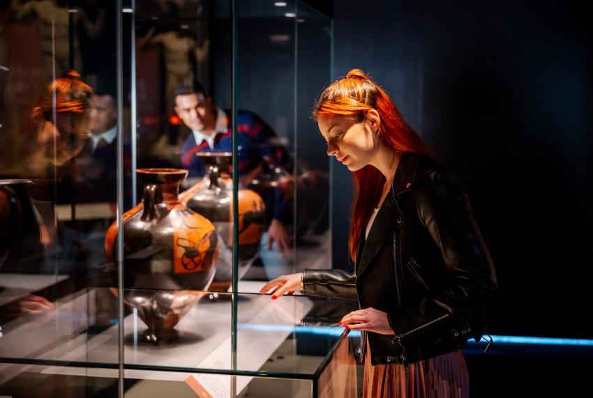 A red-haired girl looks at Ancient Greek objects in a museum showcase