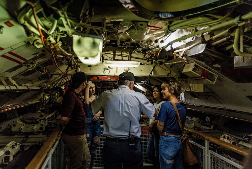 People gather around a tour leader inside a submarine