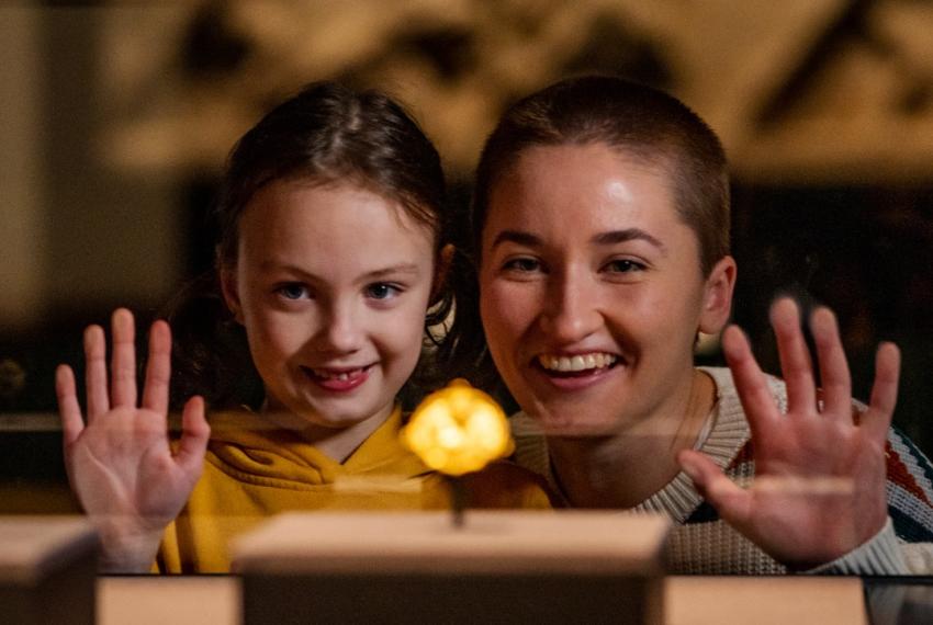 A child and an adult look with excitement at a gold object in a museum showcase