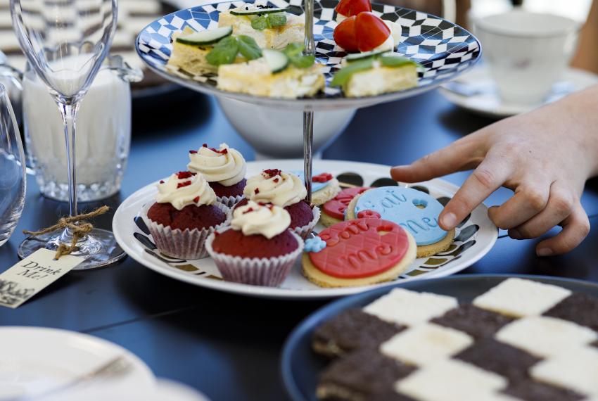 biscuits cakes and treats are on a high tea stack of plates. A hand reaches out to take a treat