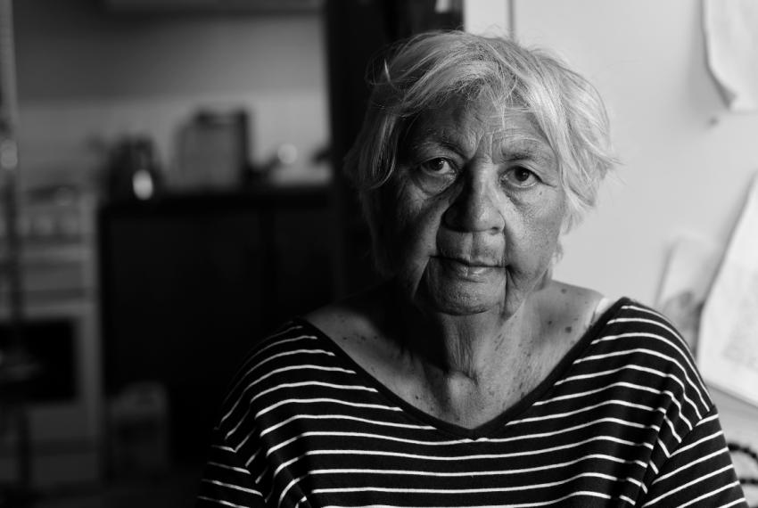 A black and white image of elderly Noongar woman Laurel Nannup who looks directly into the camera. She wears a black and white striped shirt.