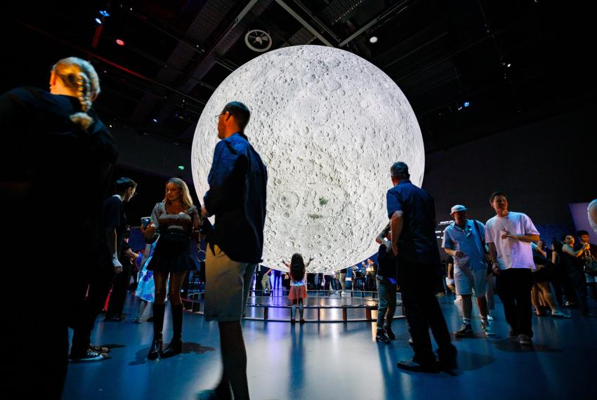 Large, impressive moon installation suspended in mid-air within an exhibition space with people walking around