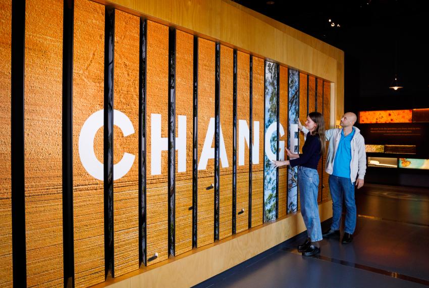 Two people interact with a wooden panel displaying the word "CHANGES" in large white letters.