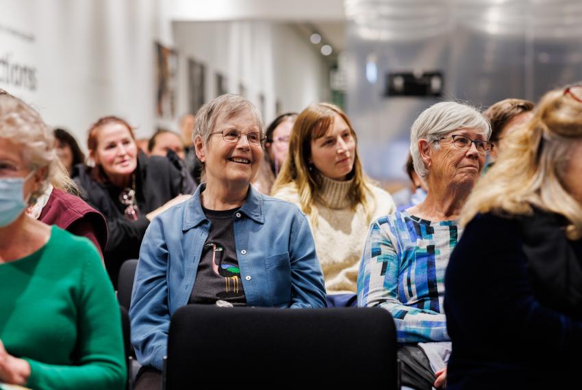 People seated in a lecture setting, with three stylishly dressed older people featured in the image foreground.