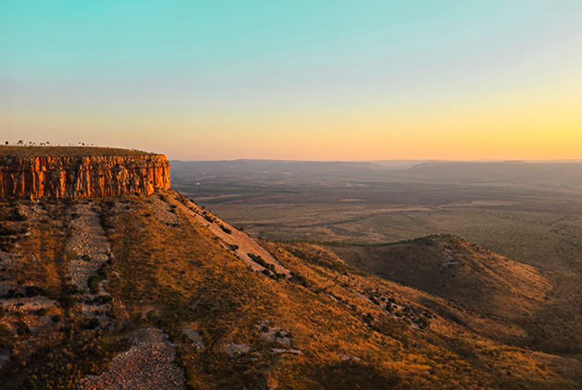 Vast landscape at sunset with a golden-lit plateau and rolling hills.