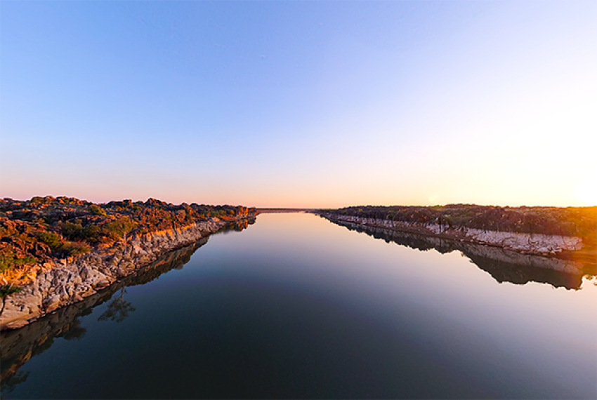 Calm river at sunrise or sunset with rocky banks and a gradient sky.