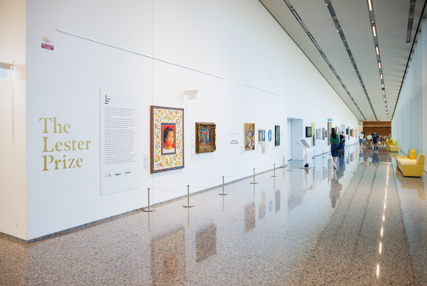 A modern museum corridor with "The Lester Prize" exhibition, showcasing various framed artworks on white walls.
