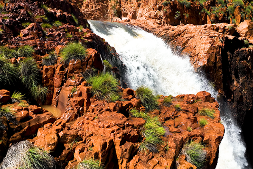 Waterfall cascading over red rock formations with green grass patches.