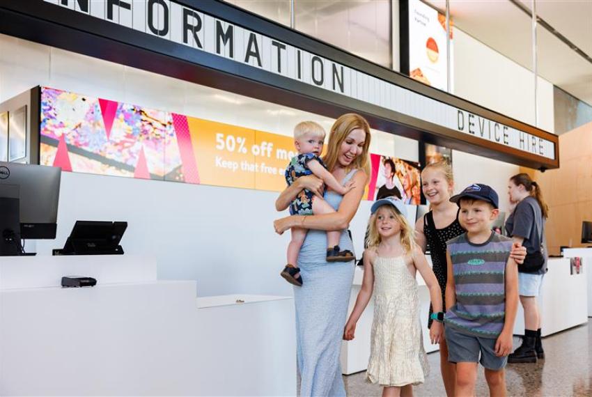 Family leaving front counter with 50 per cent off messaging in the background