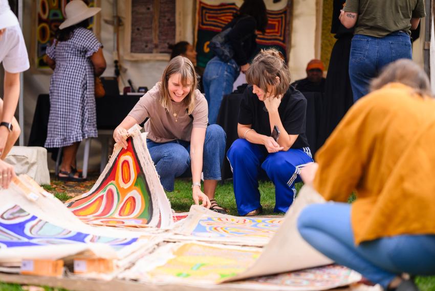 Two people crouching and flipping through a stack of canvas artworks