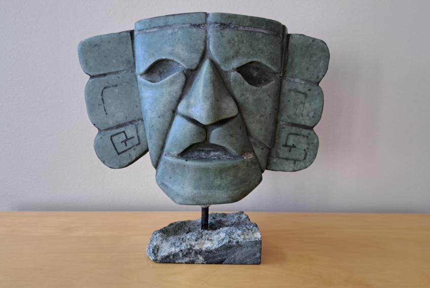 Stone sculpture of a stylized human face with geometric carvings, mounted on a base.