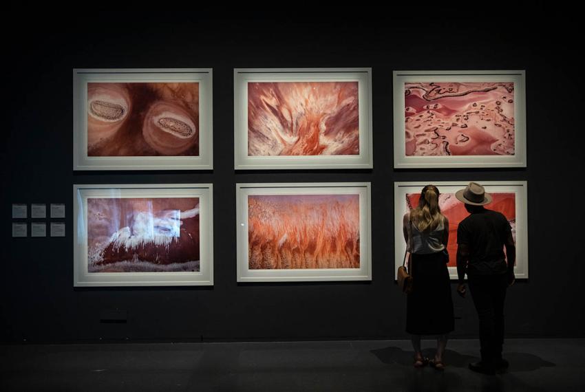 Two people stand looking at six large scale aerial photographs in a gallery