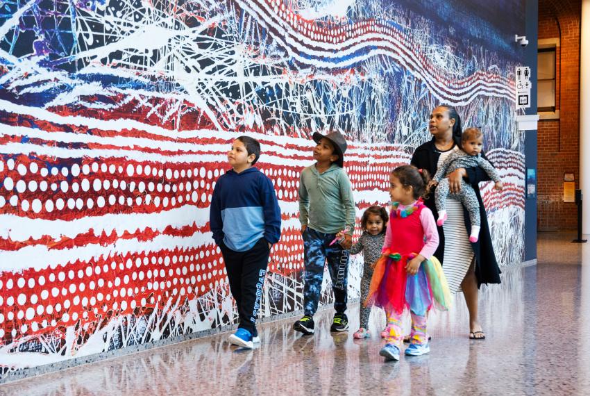 A family walking through the Museum beside a large-scale artwork print.