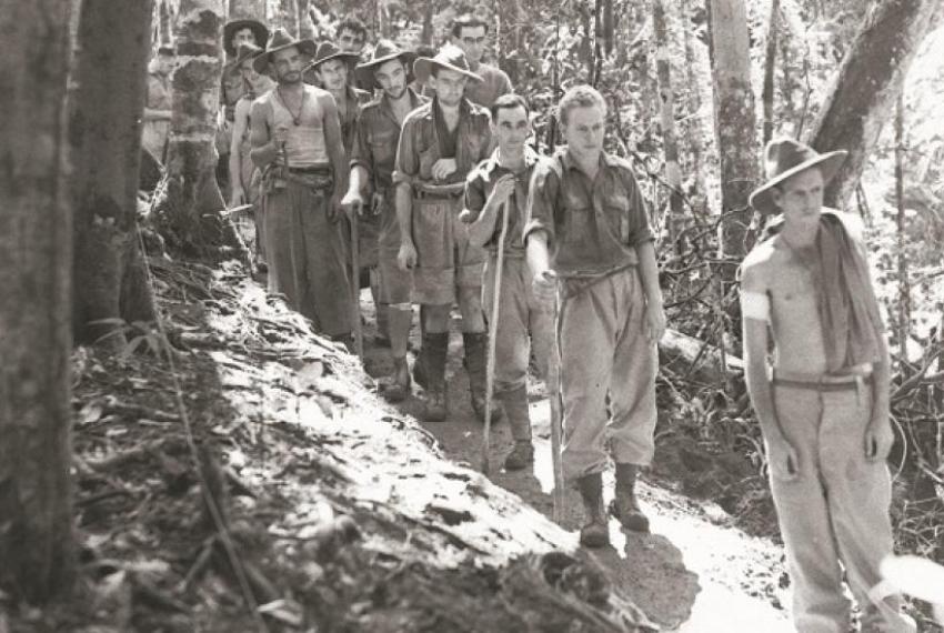 a black and white picture of soldiers walking in a line outdoors