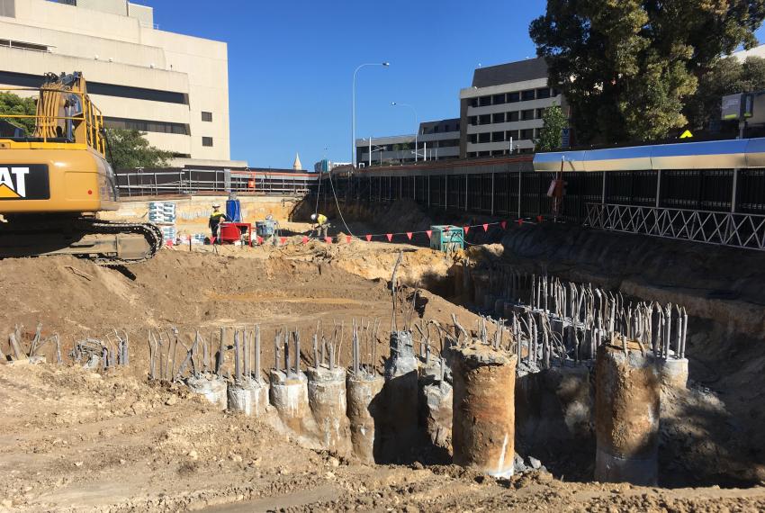 A construction site with a large hole in the ground revealing concrete poles