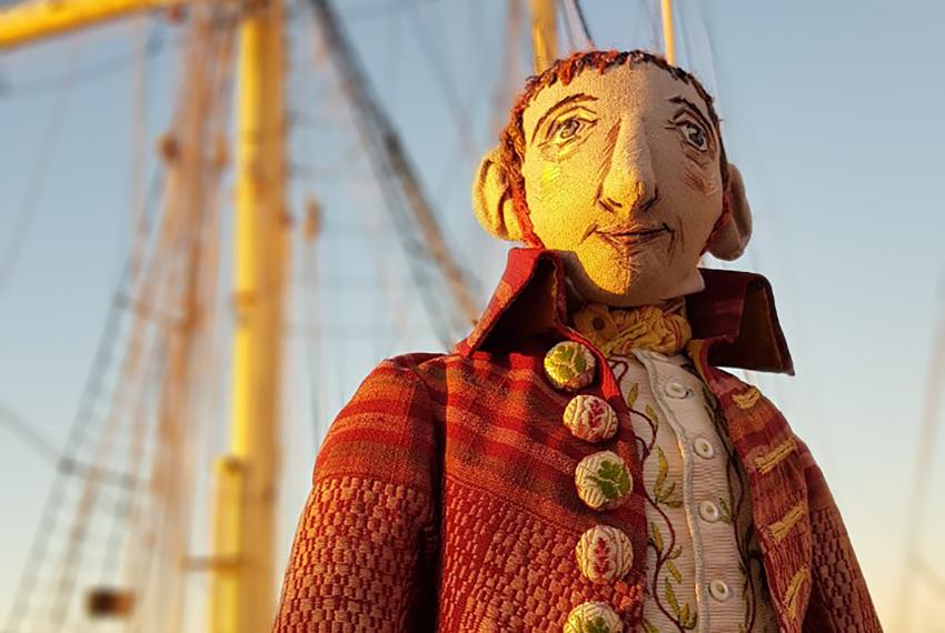 A handcrafted puppet of an 18th Century botanist with a boat in the background.