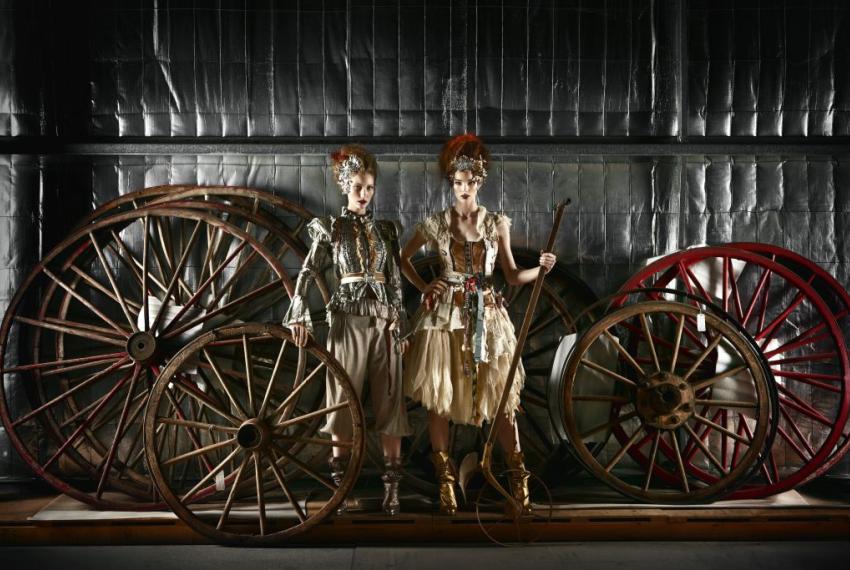 Two female models posing in front of large wheels