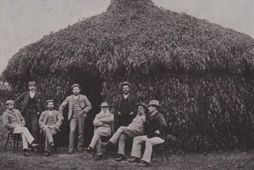 A crowd of people in front a large grass hut