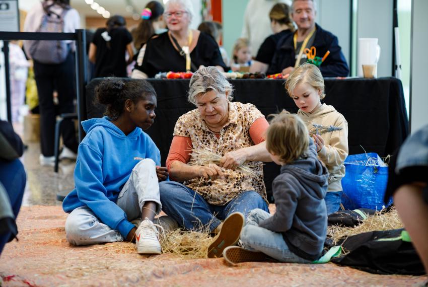 Women sitting with three children of varying age, demonstrating weaving.